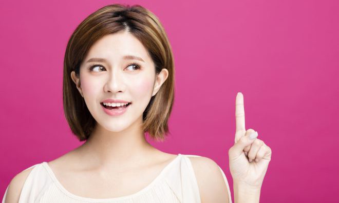 young woman pointing to somewhere, isolated on pink background